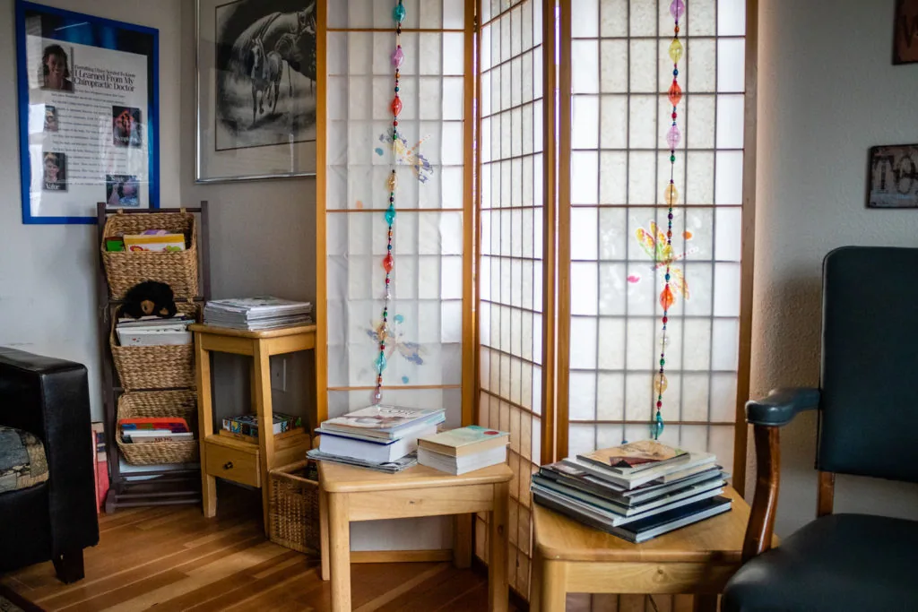 Cozy office interior with wooden furniture, beaded window hangings, stacked books, wicker storage baskets, and framed wall displays