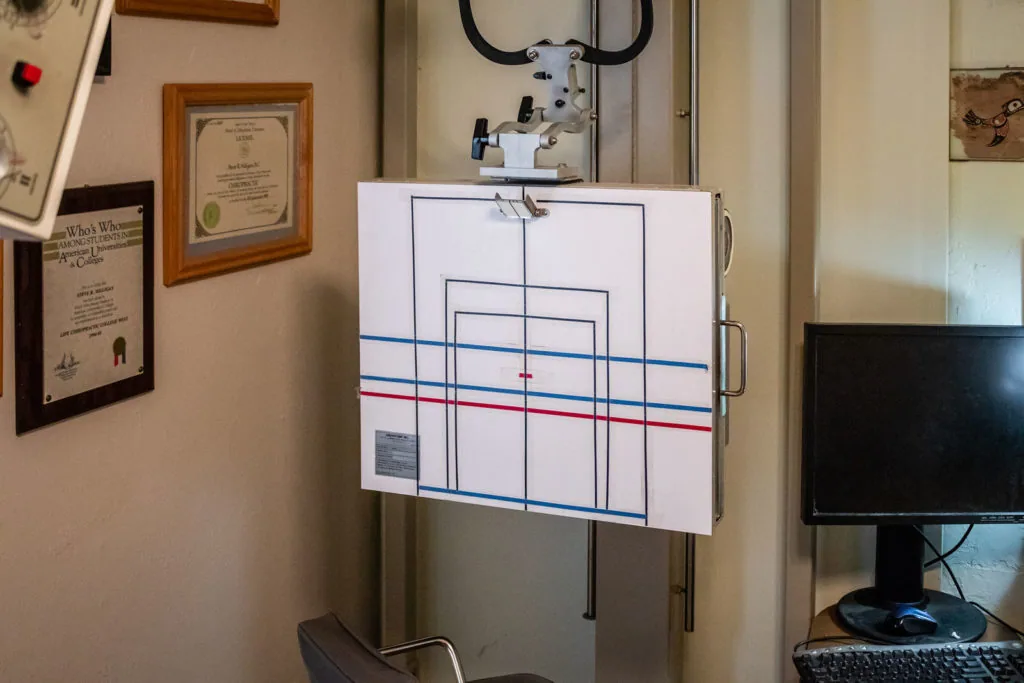 Chiropractic spinal analysis diagram mounted on wall with grid lines and colored markings in medical office