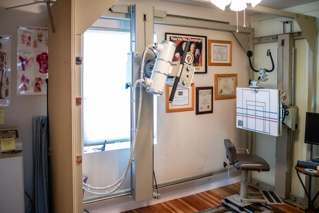 Medical examination room with hyperbaric chamber, framed certifications on wall, and examination equipment