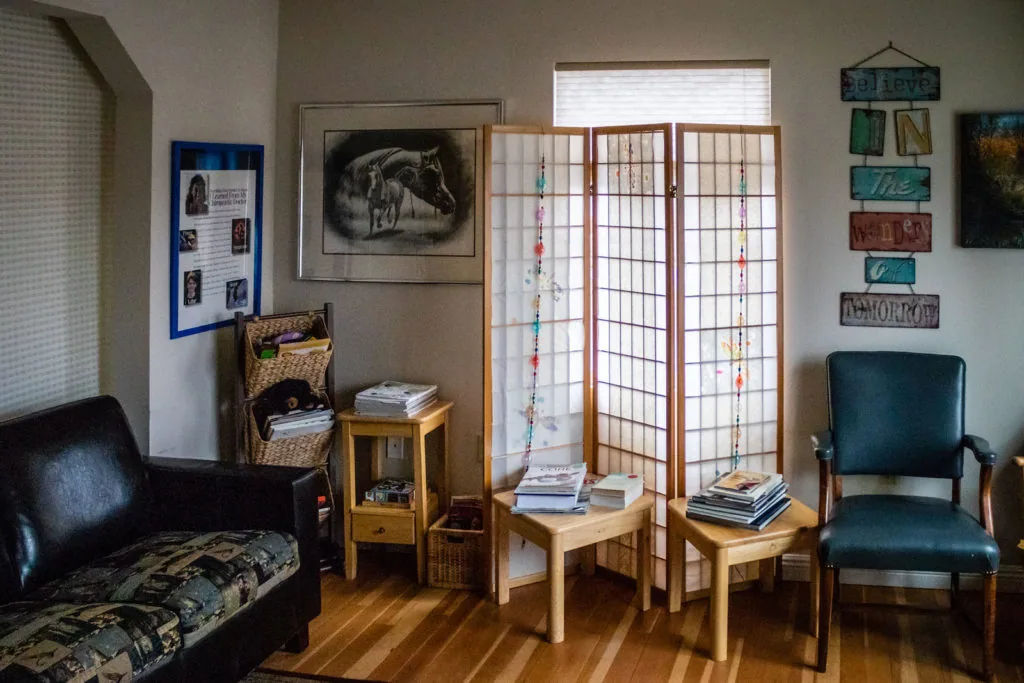 Chiropractic office waiting room with wood chairs, wooden divider screen, treatment posters, and decorative wall signage