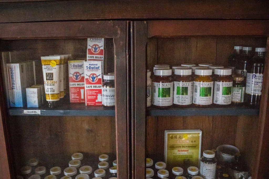 Wooden cabinet displaying vintage health and wellness products including jars, tubes, and bottles with red and white labels