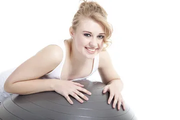Woman leaning over an exercise ball with hands positioned on top, smiling at camera