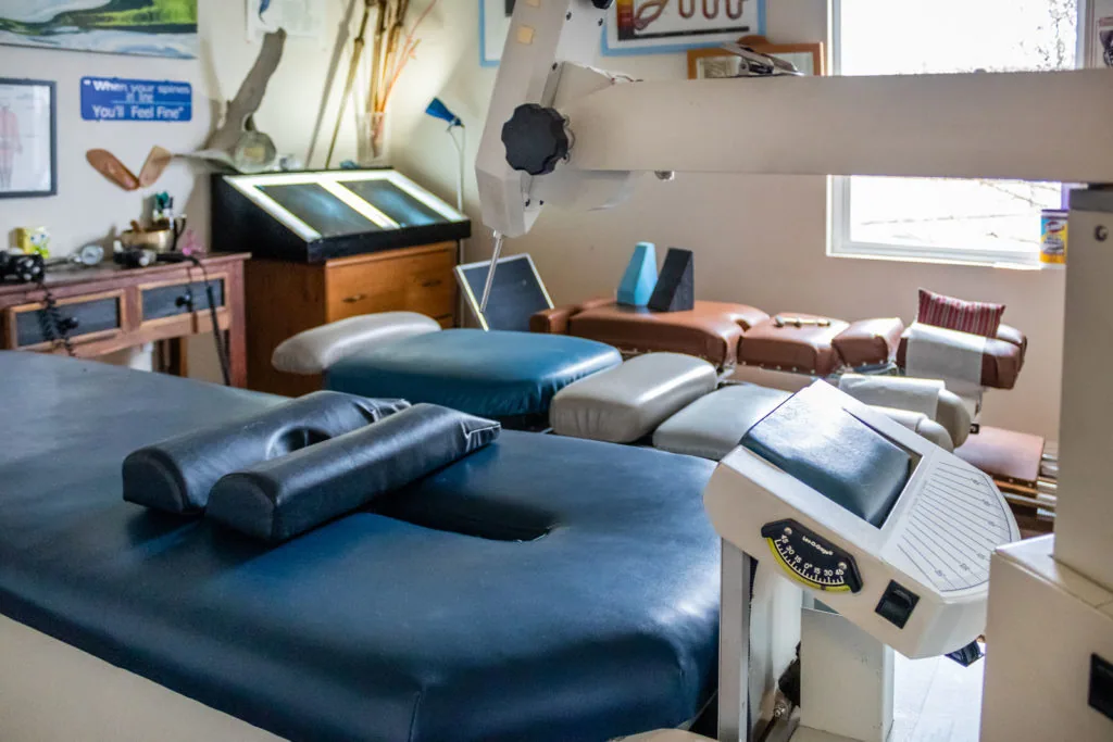 Chiropractic treatment room with blue adjusting table, massage equipment, and therapeutic supplies.
