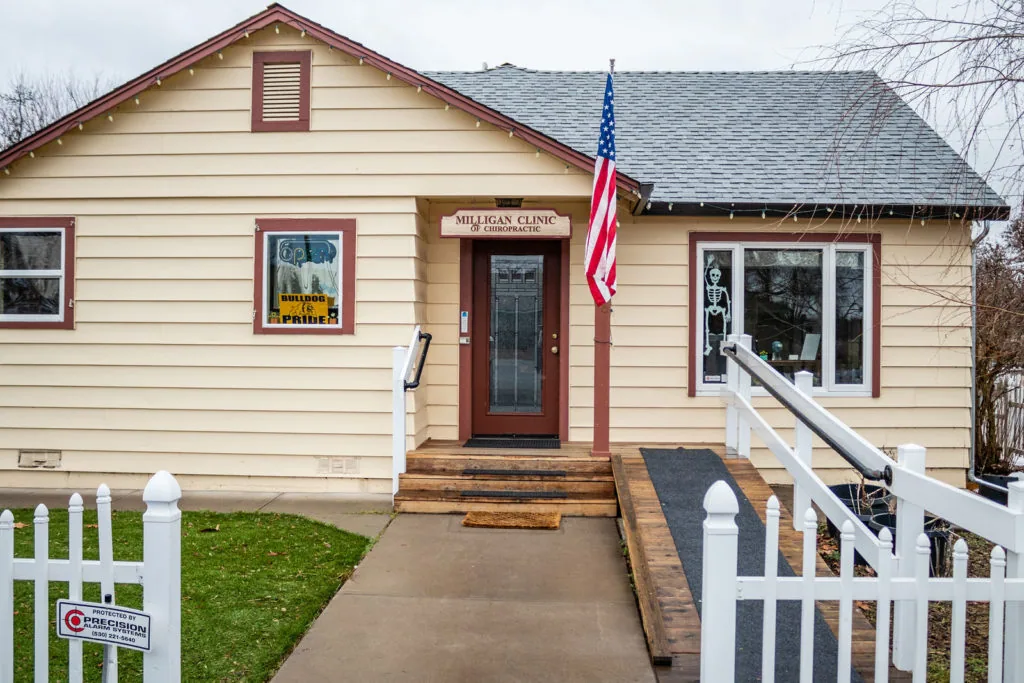 Cream-colored single-story chiropractic clinic building with red trim, white railings, and American flag at entrance