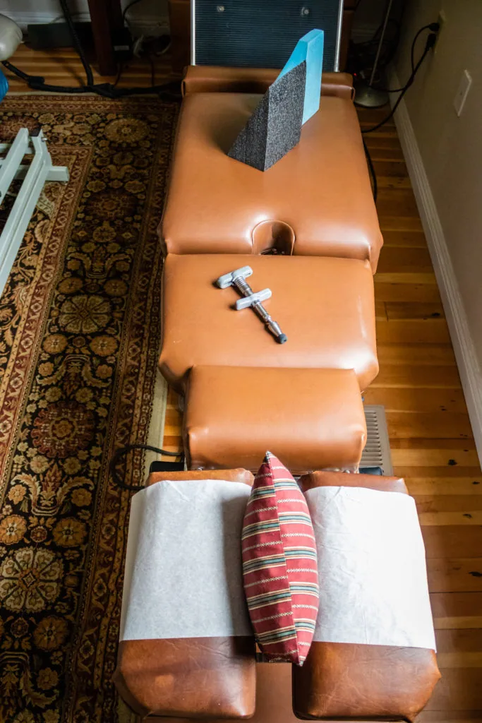 Orange leather chiropractic treatment table with adjustment headrest, white towels, and red striped neck pillow in office setting