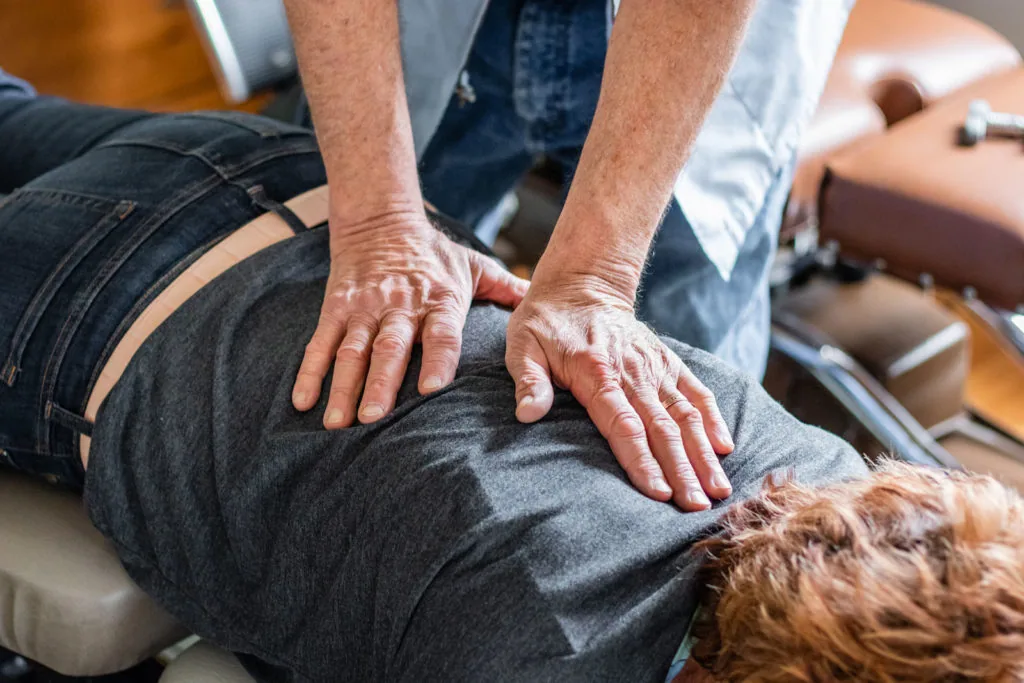 Chiropractor performing spinal adjustment on patient's lower back while patient lies face down