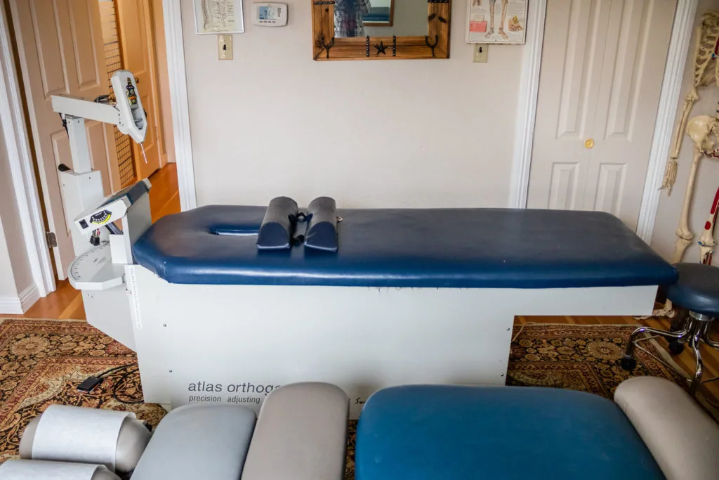 Chiropractic treatment table with blue padded surface and white base in clinical office space